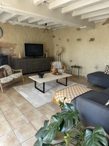 Salon spacieux et lumineux du gîte Le Logis de l'Orfosse avec poutres apparentes et décoration naturelle.